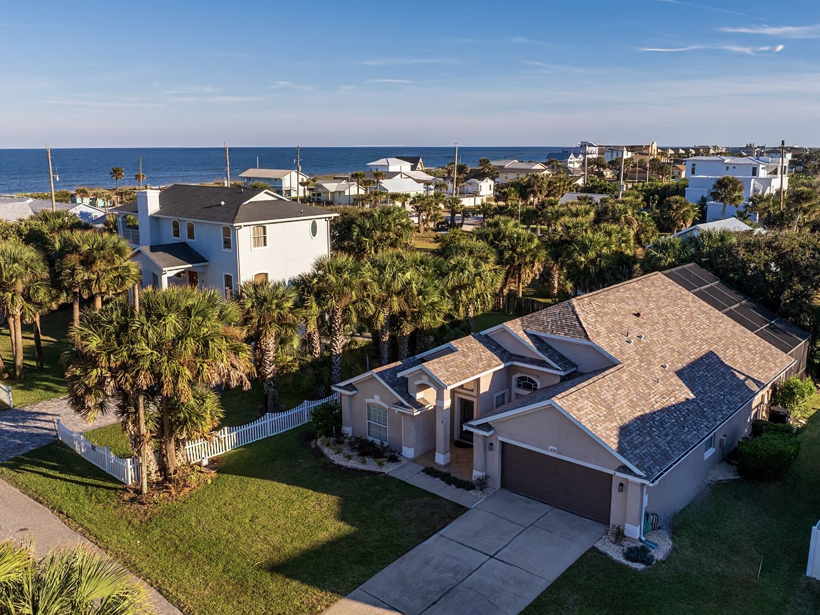 Aerial view of two of the Boom Mortgage team’s Vilano Beach vacation rentals — a single-storey home with a screened pool and a two-storey house behind it — with the beach houses of Vilano Beach and the Atlantic Ocean along the horizon
