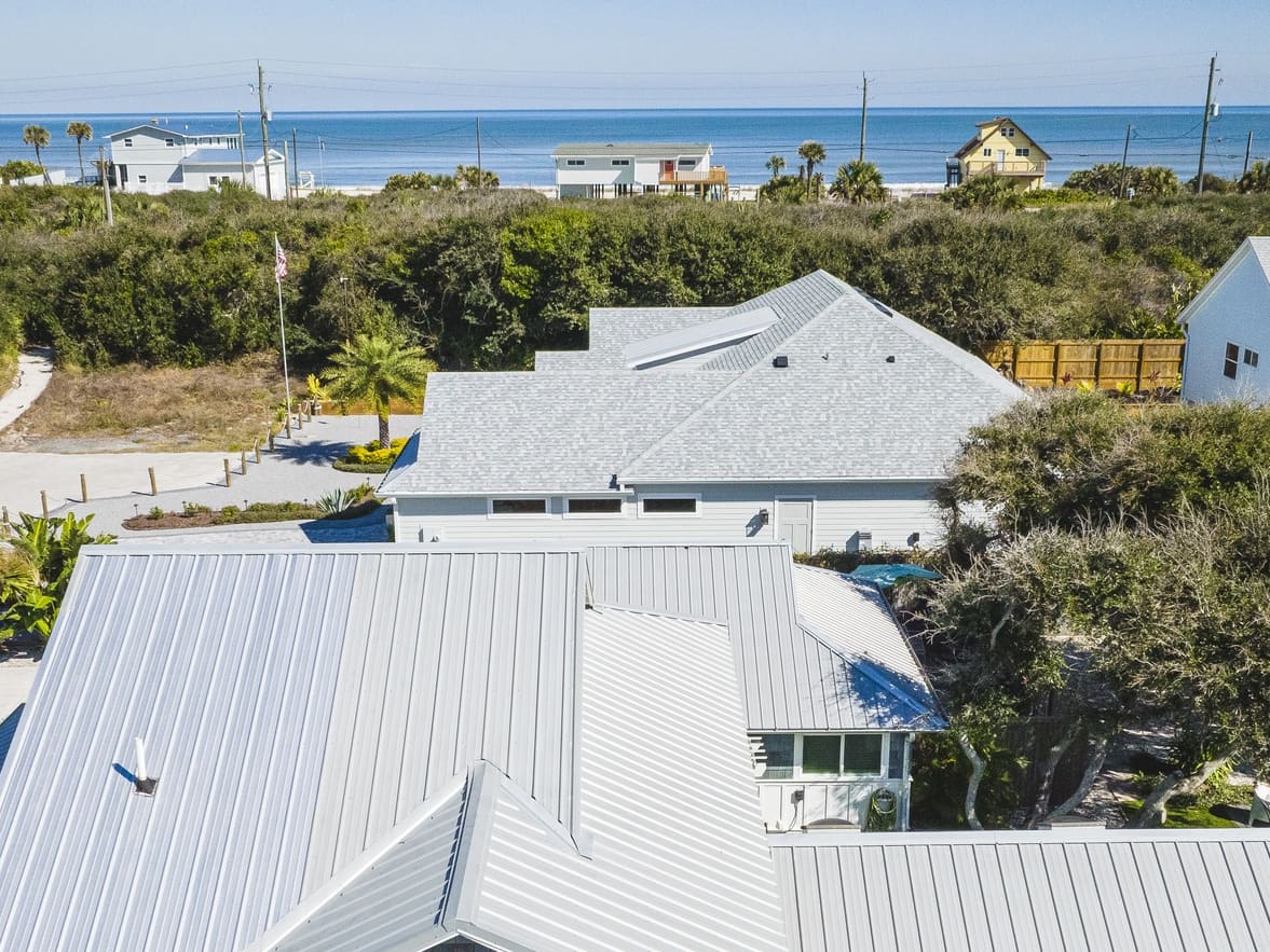 Aerial view over the metal roof of a shingle-sided beach house toward the dunes, the oceanfront houses and the Atlantic Ocean at Vilano Beach